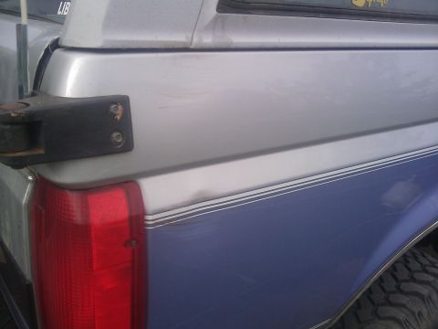 1996 Ford Bronco - Rear view of a blue and silver Ford Bronco showing damage and a tow hitch mount.