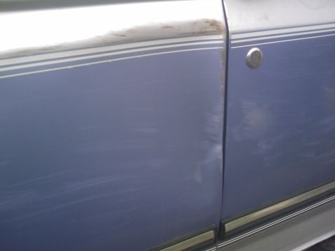 1996 Ford Bronco - Close-up of damage on a vehicle's side door, showing a dent and numerous scratches.
