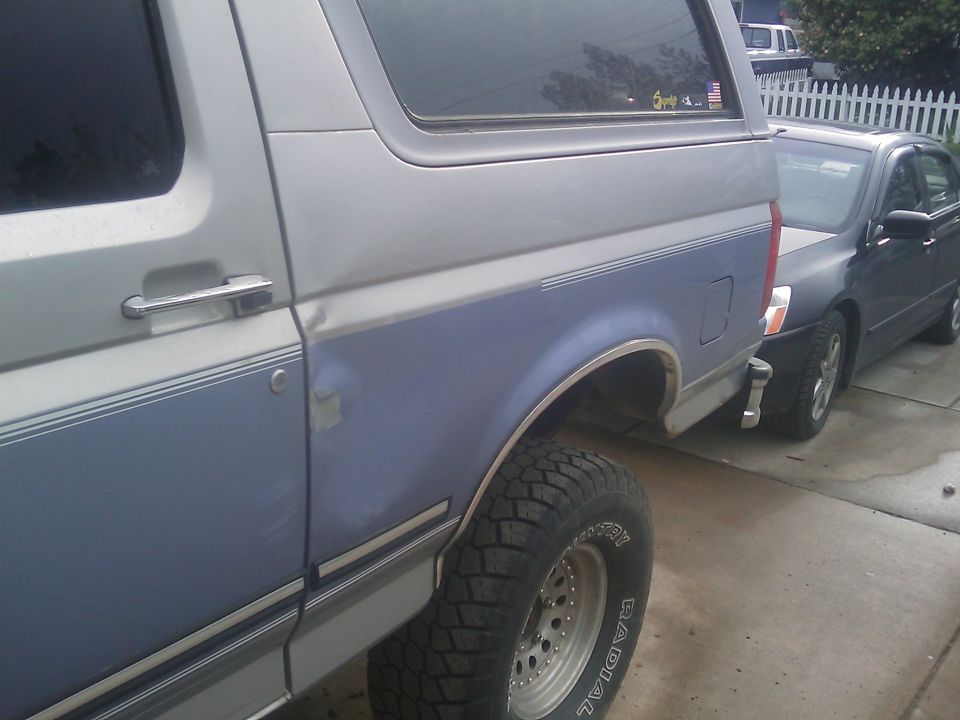 Side view of a 1996 Ford Bronco with blue and silver paint. Another car is parked behind it
