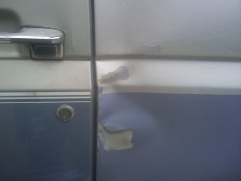 1996 Ford Bronco - Close-up of a damaged vehicle door showing dents and peeling paint.