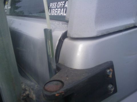 1996 Ford Bronco - Close-up of a silver SUV's rear quarter panel, showing a mounting bracket and a political sticker on the window.