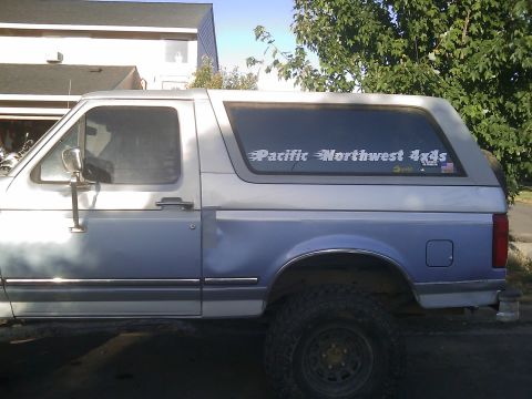 1996 Ford Bronco - This two-tone blue and silver SUV, likely a Ford Bronco from the 1990s, features a camper shell and a 'Pacific Northwest 4x4s' decal on the…