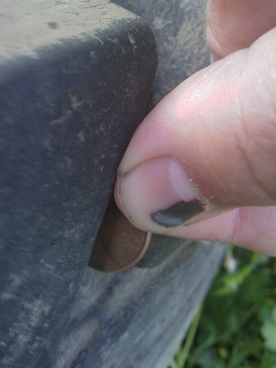 Finger pressing on a tire sidewall, showing a penny for scale
