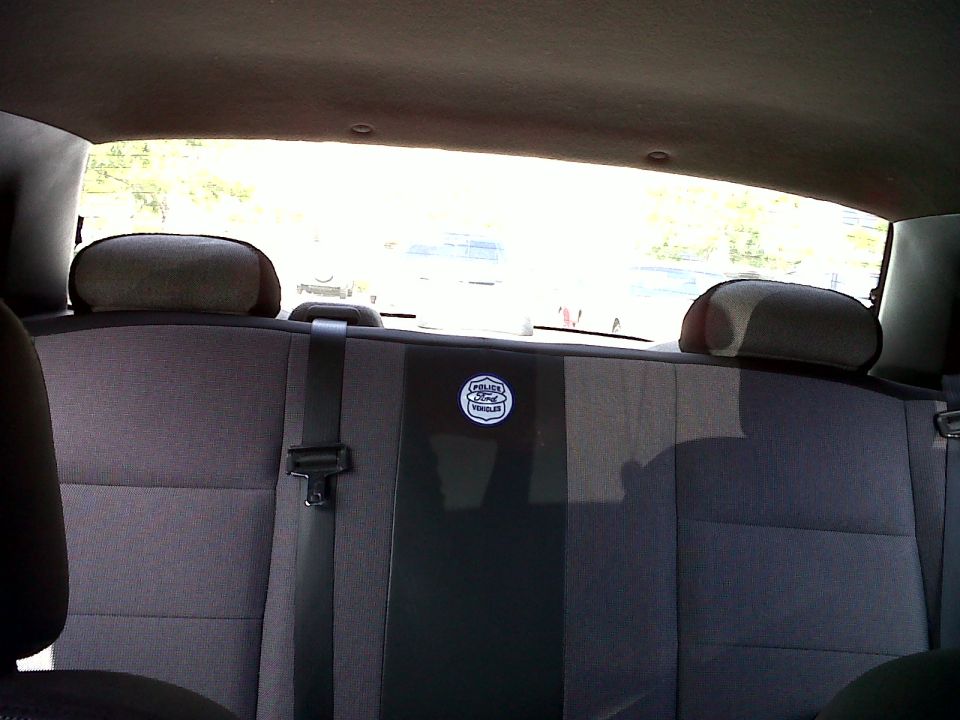 Back seat with a "Police Ford Vehicles" emblem on the center seatback. Other cars visible through the rear window