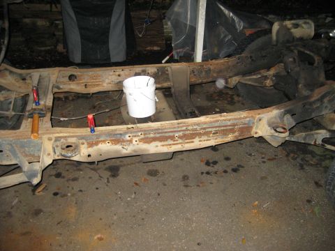 1988 Ford Bronco - The heavily rusted frame of a vehicle sits on the ground, showing signs of disrepair and potential restoration work.