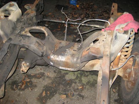1988 Ford Bronco - Close-up view of a heavily rusted vehicle frame and suspension parts, possibly undergoing restoration.