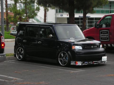 1998 Ford Crown Victoria - A black hatchback is parked next to a red van with a bakery logo.