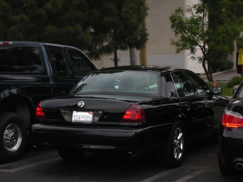 1998 Ford Crown Victoria - A black 1998 Ford Crown Victoria is seen from the rear, parked in a lot next to a dark pickup truck.