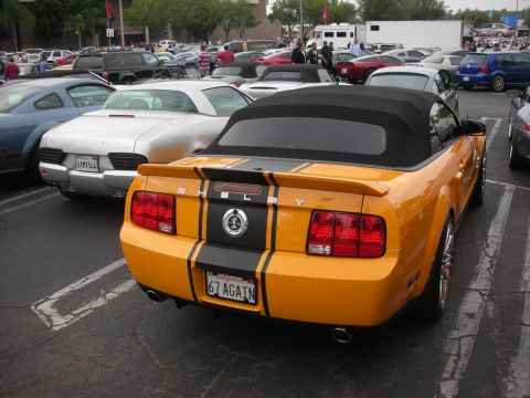 1998 Ford Crown Victoria - A bright orange convertible Mustang with racing stripes is parked in a lot full of other vehicles.