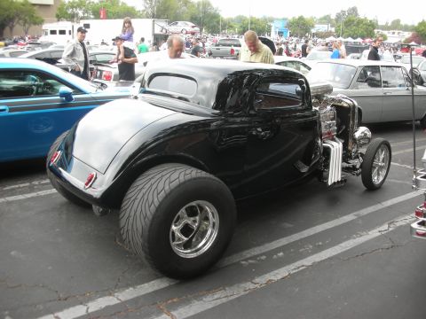 1998 Ford Crown Victoria - A custom black hot rod coupe with a prominent engine and large rear tires is parked at an outdoor event.