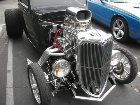1998 Ford Crown Victoria - A custom hot rod with a prominent chrome grille and engine dominates the foreground, with a modern blue car in the background.