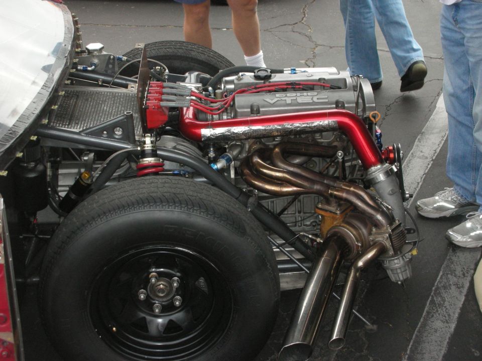 Engine bay of a custom car with VTEC engine, red intake, and custom exhaust