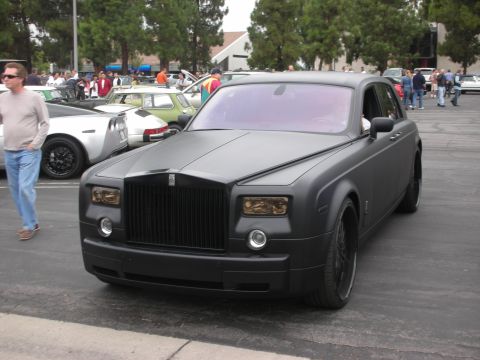 1998 Ford Crown Victoria - A matte black Rolls-Royce Phantom is parked at an outdoor gathering with other vehicles present.