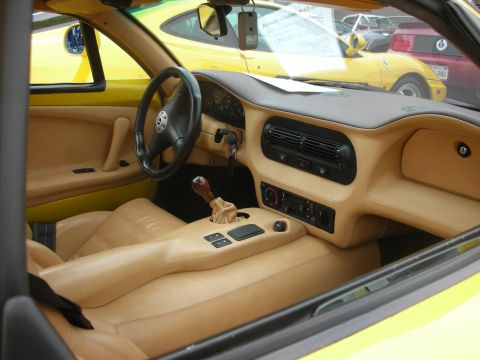 1998 Ford Crown Victoria - Interior view of a yellow car with tan upholstery, showing the dashboard, steering wheel, and gear shifter, with other vehicles visible out…