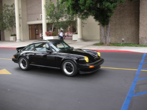 1998 Ford Crown Victoria - A black Porsche 911 with distinctive yellow headlights is captured in motion on a paved surface.