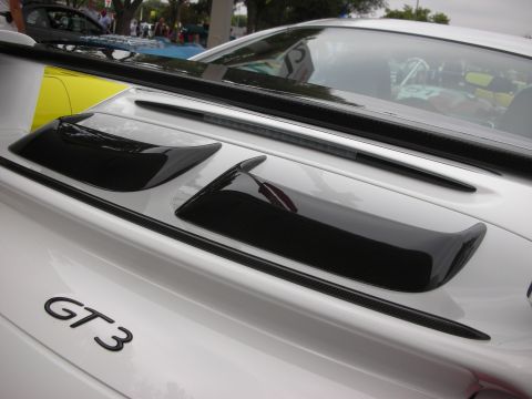 1998 Ford Crown Victoria - The rear decklid of a white Porsche GT3 features carbon fiber accents and a prominent spoiler, with other vehicles visible in the backgroun…