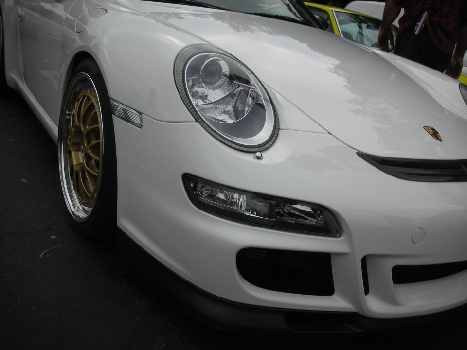 White Porsche 911 front view with gold wheels and a yellow car in the background