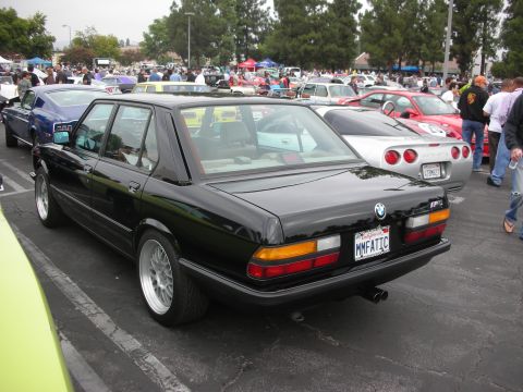 1998 Ford Crown Victoria - Black BMW E28 M5 sedan at a car meet, with a silver Corvette in the background.