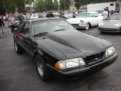 1998 Ford Crown Victoria - A black Ford Mustang is parked at an outdoor car meet with other vehicles and attendees visible.