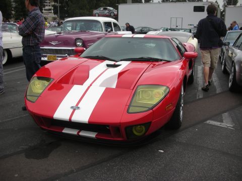 1998 Ford Crown Victoria - A red Ford GT with white racing stripes is the focus of this photo, with other vehicles and attendees in the background.