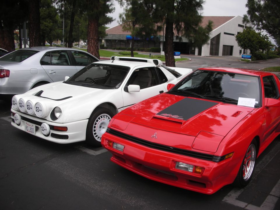 White rally car with four fog lights and a red sports car parked side-by-side