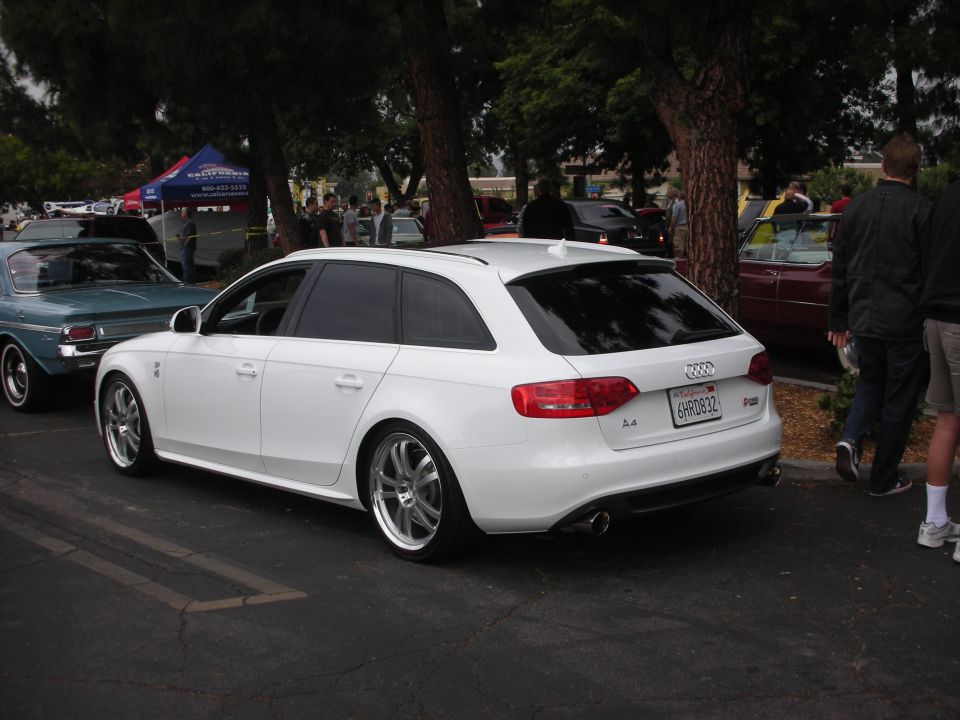 White Audi A4 wagon parked next to a blue classic car. People and tents in background