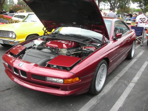 1998 Ford Crown Victoria - A red BMW 8 Series coupe is displayed with its hood open, revealing the engine compartment, parked next to a yellow car.