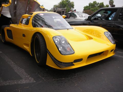 1998 Ford Crown Victoria - A bright yellow sports car is parked at an angle, with its engine cover raised, next to a black sedan.
