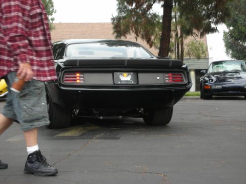 1998 Ford Crown Victoria - A black 1970 Plymouth Barracuda is seen from the rear, parked next to a dark blue Porsche.