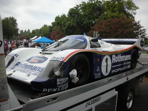 1998 Ford Crown Victoria - A Rothmans Porsche race car is being transported on a flatbed truck, with spectators in the background.