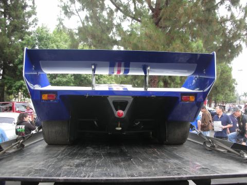 1998 Ford Crown Victoria - A blue race car with a prominent rear wing is seen from behind, loaded onto a flatbed truck.