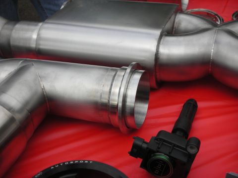 1998 Ford Crown Victoria - Custom exhaust components and an ignition coil are displayed on a red surface, suggesting automotive customization.