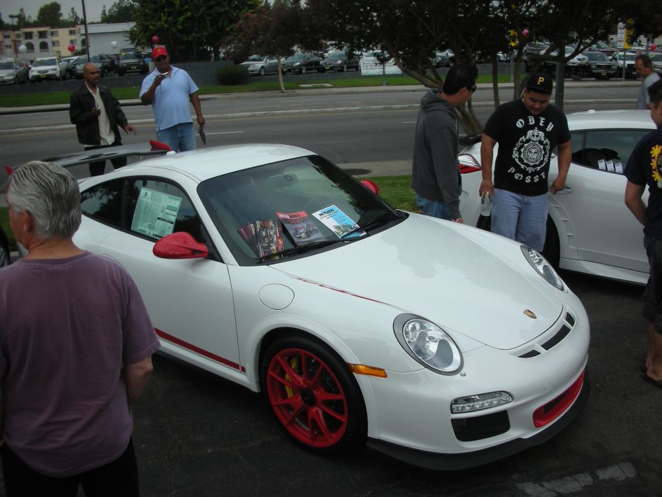 White Porsche 911 with red accents and red wheels, parked outside with people around
