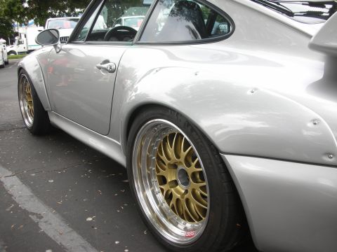 1998 Ford Crown Victoria - A silver Porsche 911 is parked on asphalt, showing its wide body kit and gold BBS wheels. Other vehicles are visible in the background.