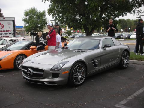 1998 Ford Crown Victoria - A silver Mercedes-Benz SLS AMG coupe is parked at a car meet, with an orange Lamborghini visible to its left.