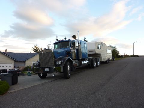 1981 Kenworth W900A - A blue semi-truck is parked on a street, towing a large trailer with a residential neighborhood in the background.