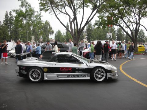 1998 Ford Crown Victoria - A silver sports car with racing decals is parked at an outdoor gathering with spectators.