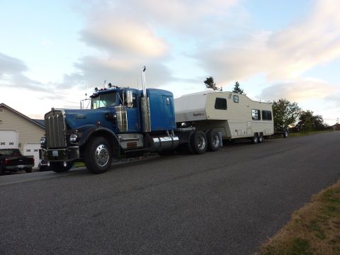 1981 Kenworth W900A - A blue semi-truck is parked on a street, towing a large white fifth-wheel recreational vehicle.