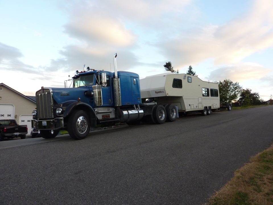 Blue semi-truck with a white fifth-wheel trailer parked on a residential street
