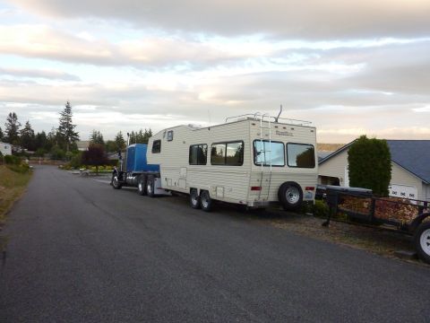 1981 Kenworth W900A - A truck tractor tows a large RV and a trailer down a paved road.