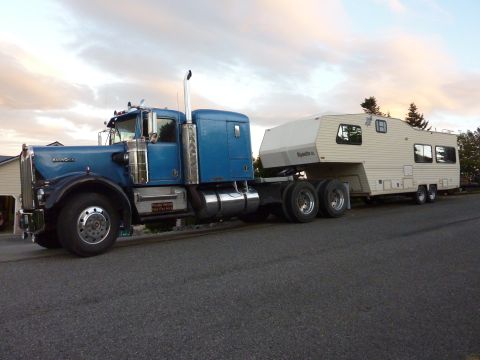 1981 Kenworth W900A - A blue 1981 Kenworth W900A semi-truck is seen from the side, towing a large white RV.