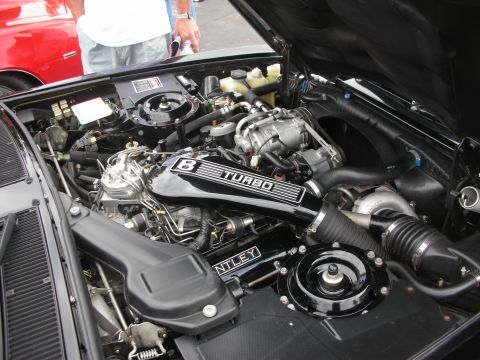 1998 Ford Crown Victoria - Close-up view of a Bentley's turbocharged engine, with a red car visible in the background.