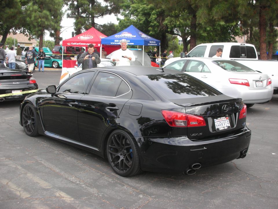 Black Lexus IS sedan with custom wheels and spoiler, parked at an outdoor car meet. License plate is KHRK919