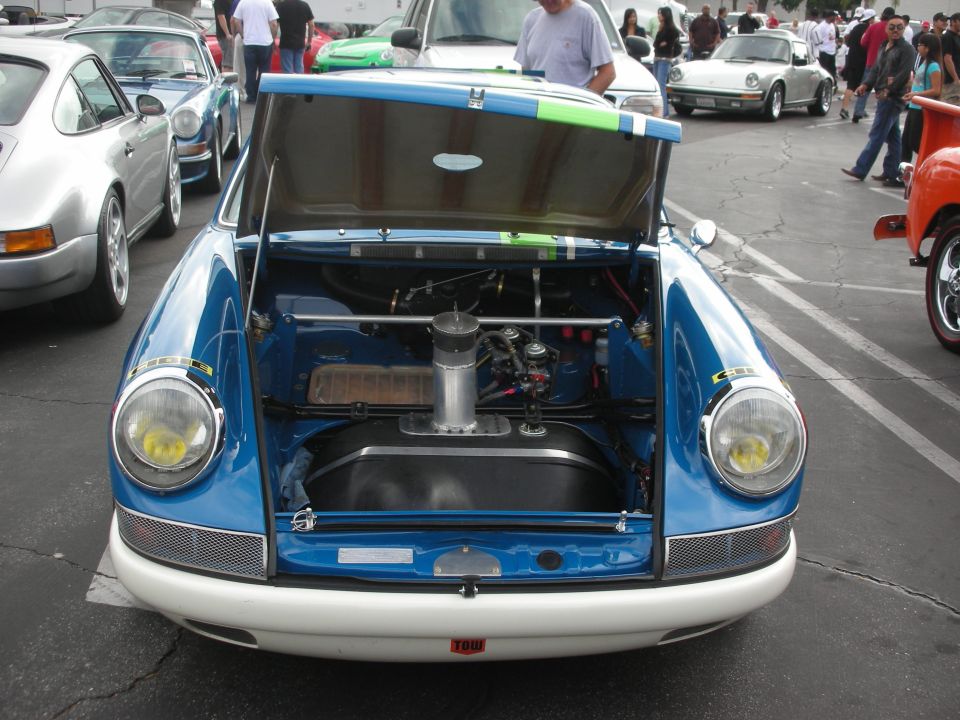 Blue and white vintage sports car front view, hood open revealing engine and fuel tank