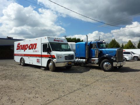 1981 Kenworth W900A - A white Snap-on truck and a blue semi-truck are parked side-by-side on a gravel lot under a cloudy sky.