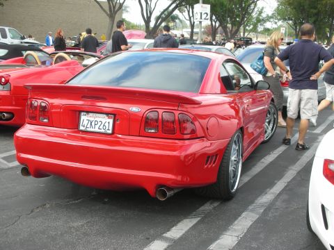 1998 Ford Crown Victoria - A bright red 1998 Ford Mustang is parked at a car meet, its rear end and custom modifications.