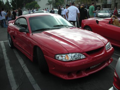 1998 Ford Crown Victoria - A red coupe with a custom body kit and hood scoops is parked in a lot.