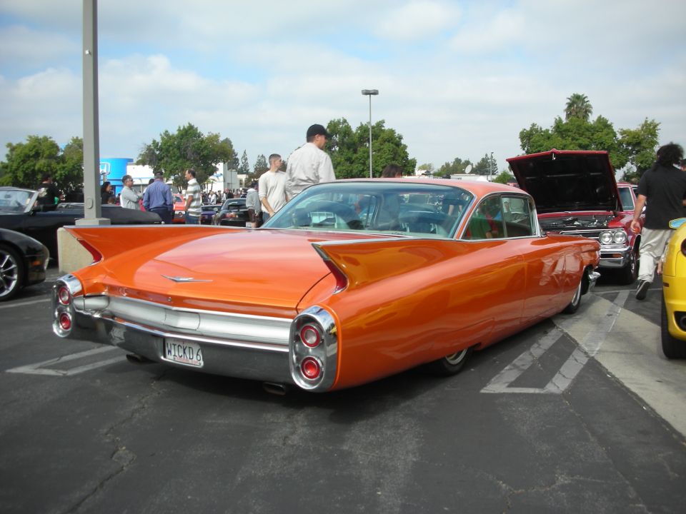 Orange 1959 Cadillac Coupe de Ville with fins and dual taillights, parked at a car meet
