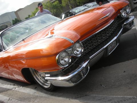 1998 Ford Crown Victoria - A man stands behind a shiny orange classic Cadillac convertible at an outdoor gathering.