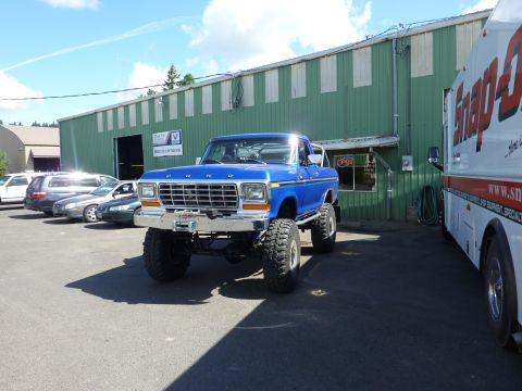 1981 Kenworth W900A - A lifted blue Ford pickup truck is parked outside a commercial building next to a white truck.